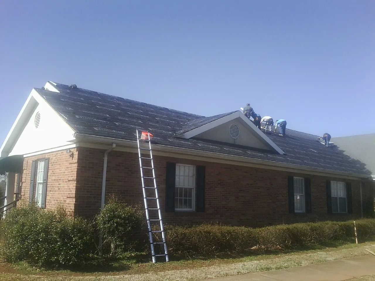 Crew tearing shingles off a brick ranch roof with a ladder set — Emergency Roof Repair work by our crew in Tendoy