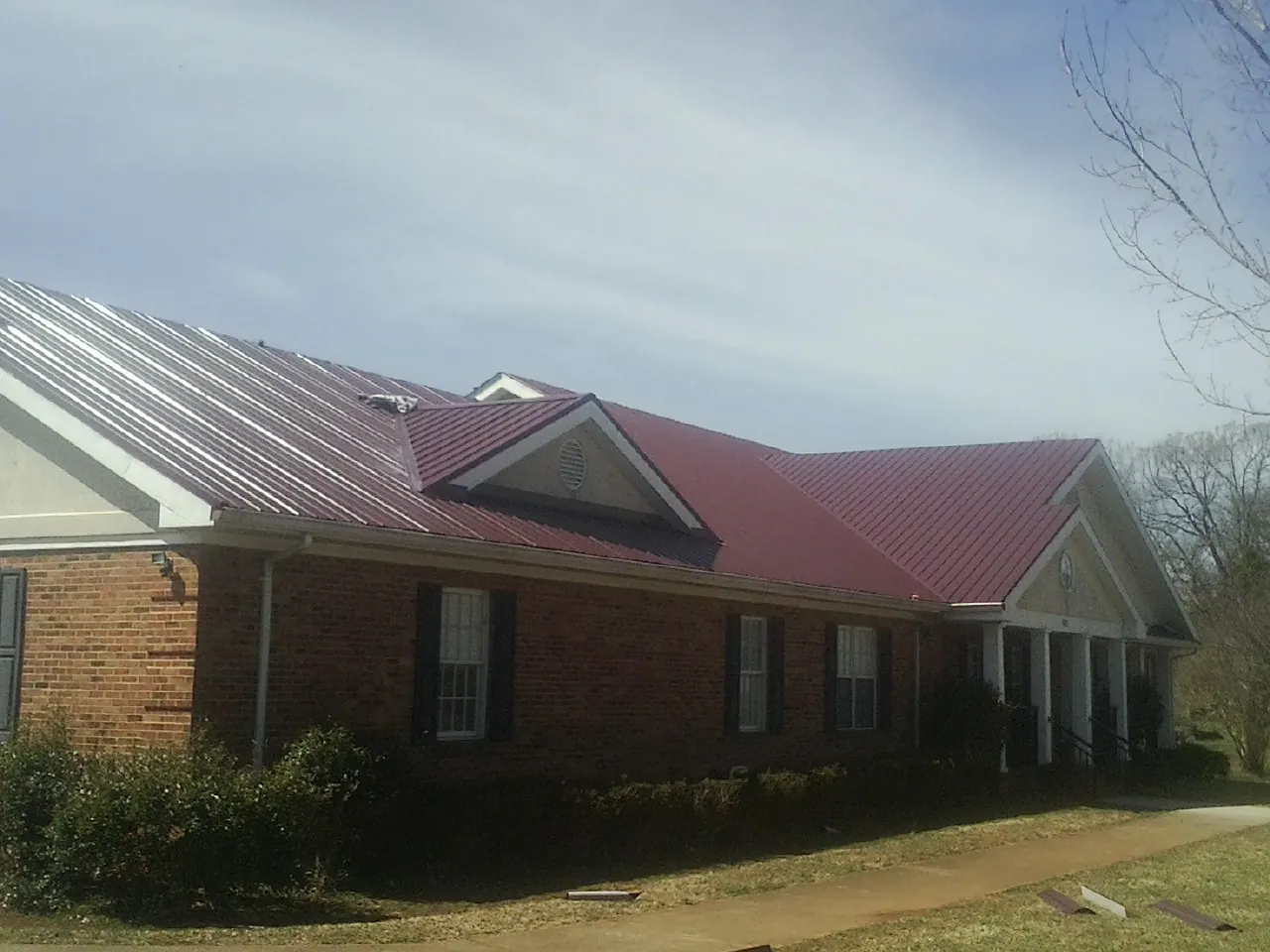 Red metal roof with gabled entries on a long brick building, from a Hail Damage Roof Repair job in Tendoy