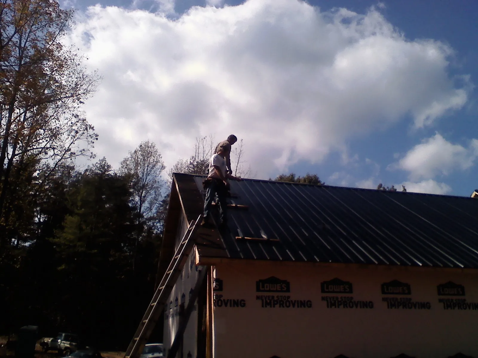 Roofer fastening dark metal panels high against a cloudy sky, from a Roof Inspection job in Tendoy