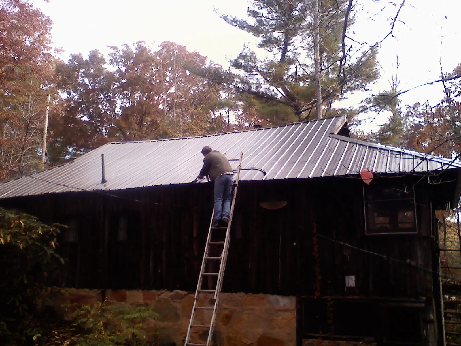 Roofer on a ladder working along the edge of a cabin metal roof in Tendoy