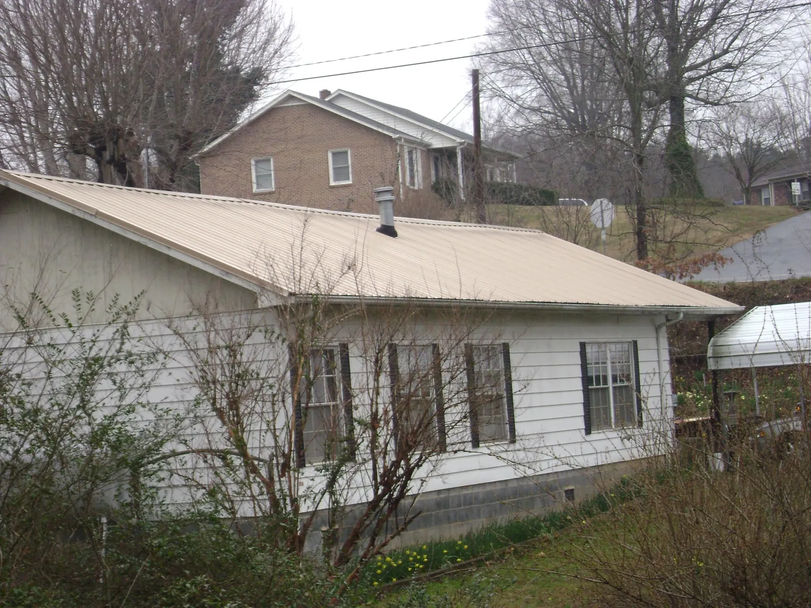 Tan metal roof on a white sided house set into a hillside — Commercial Roofing by Roofing Brothers in Tendoy